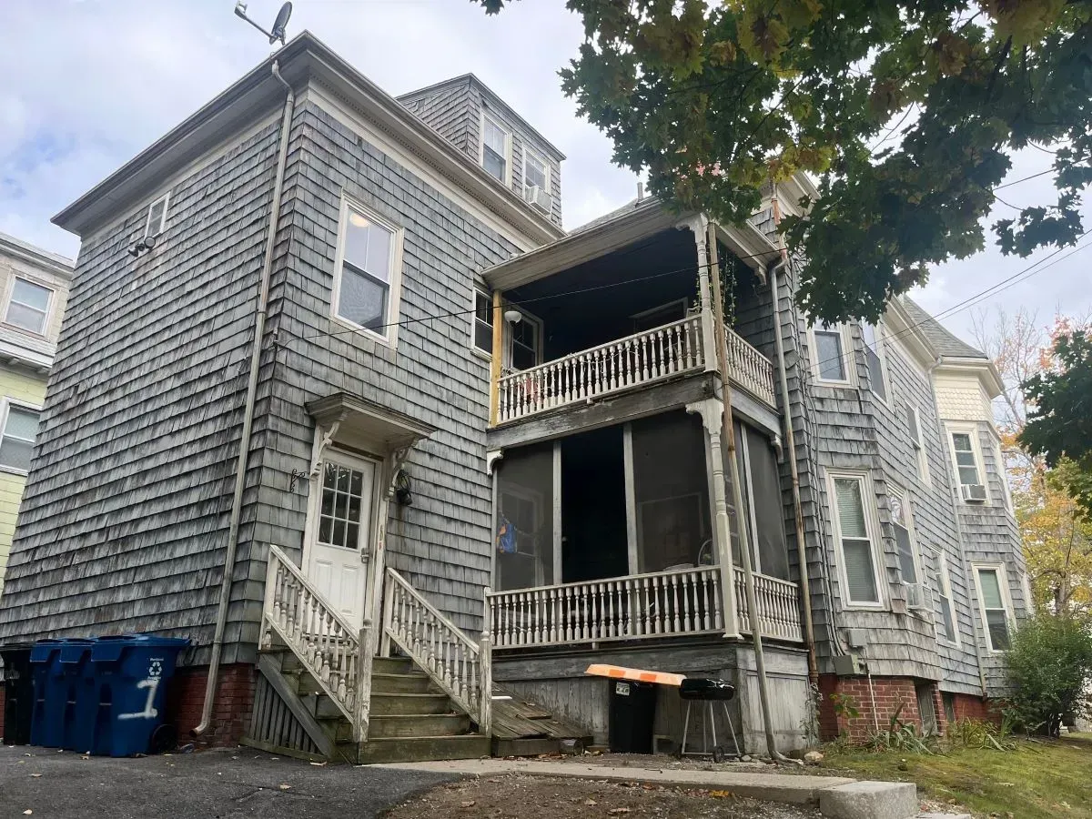 A large gray house with a screened in porch and stairs.