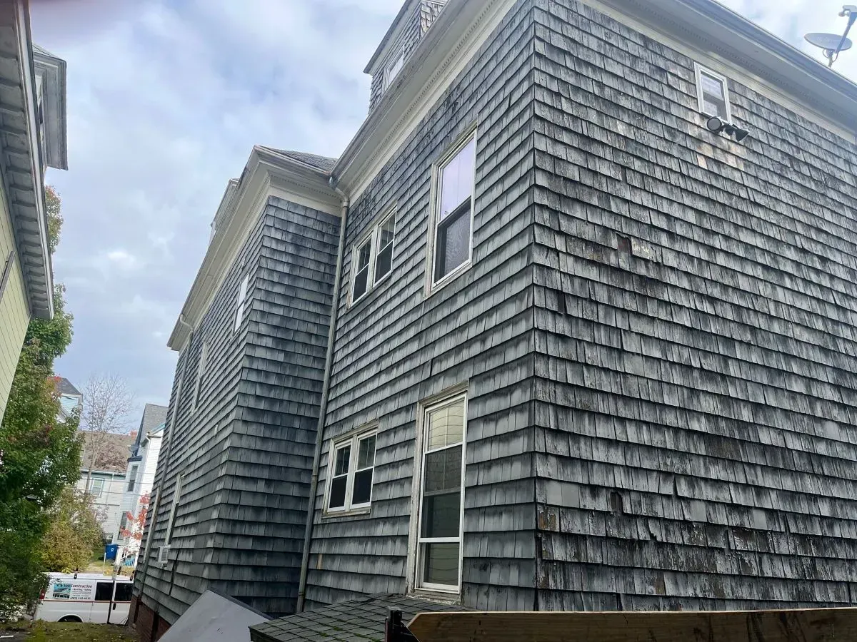 A large gray building with a shingle roof and a lot of windows.