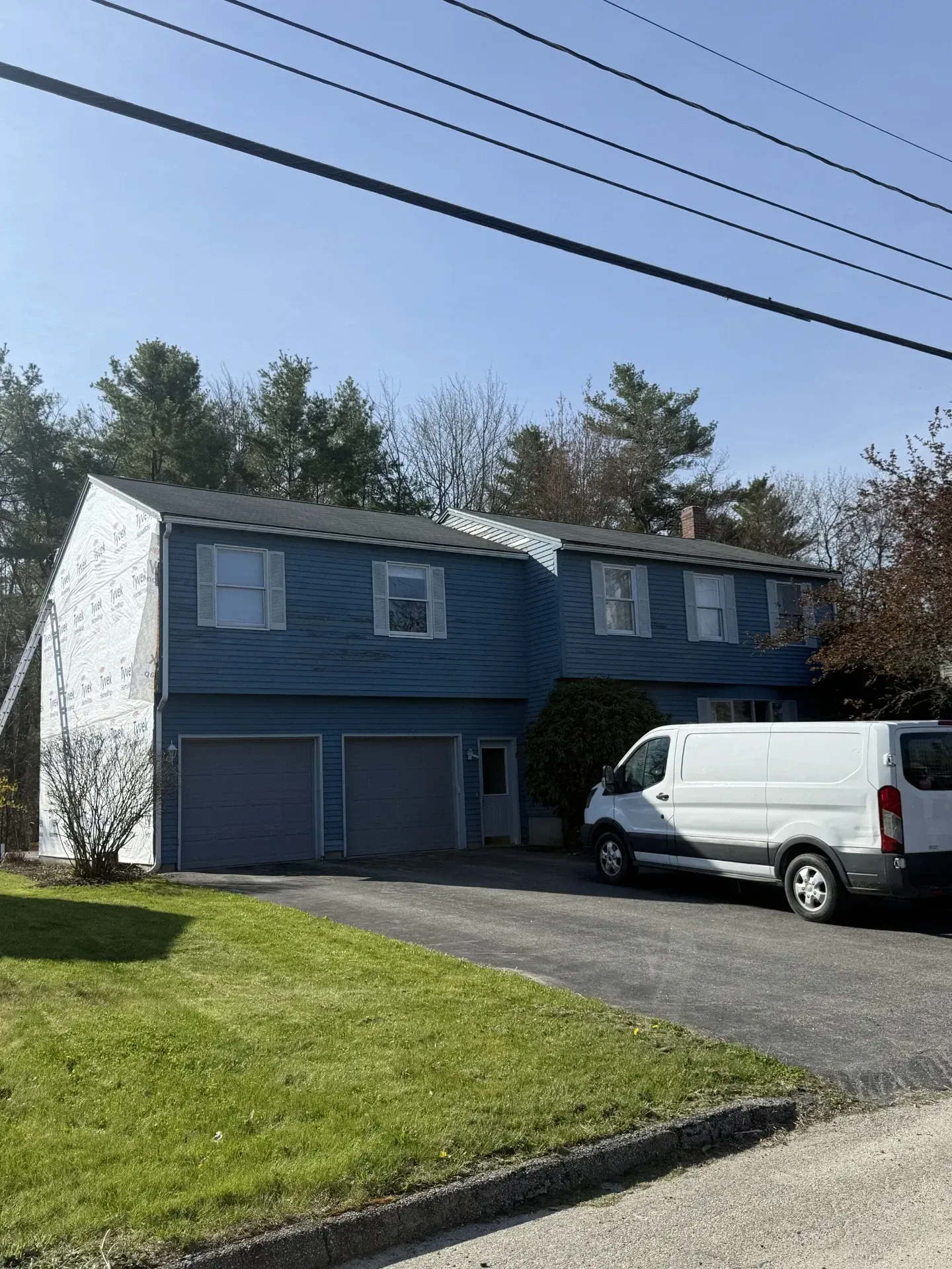 Two-story blue house with white van parked in driveway on a sunny day