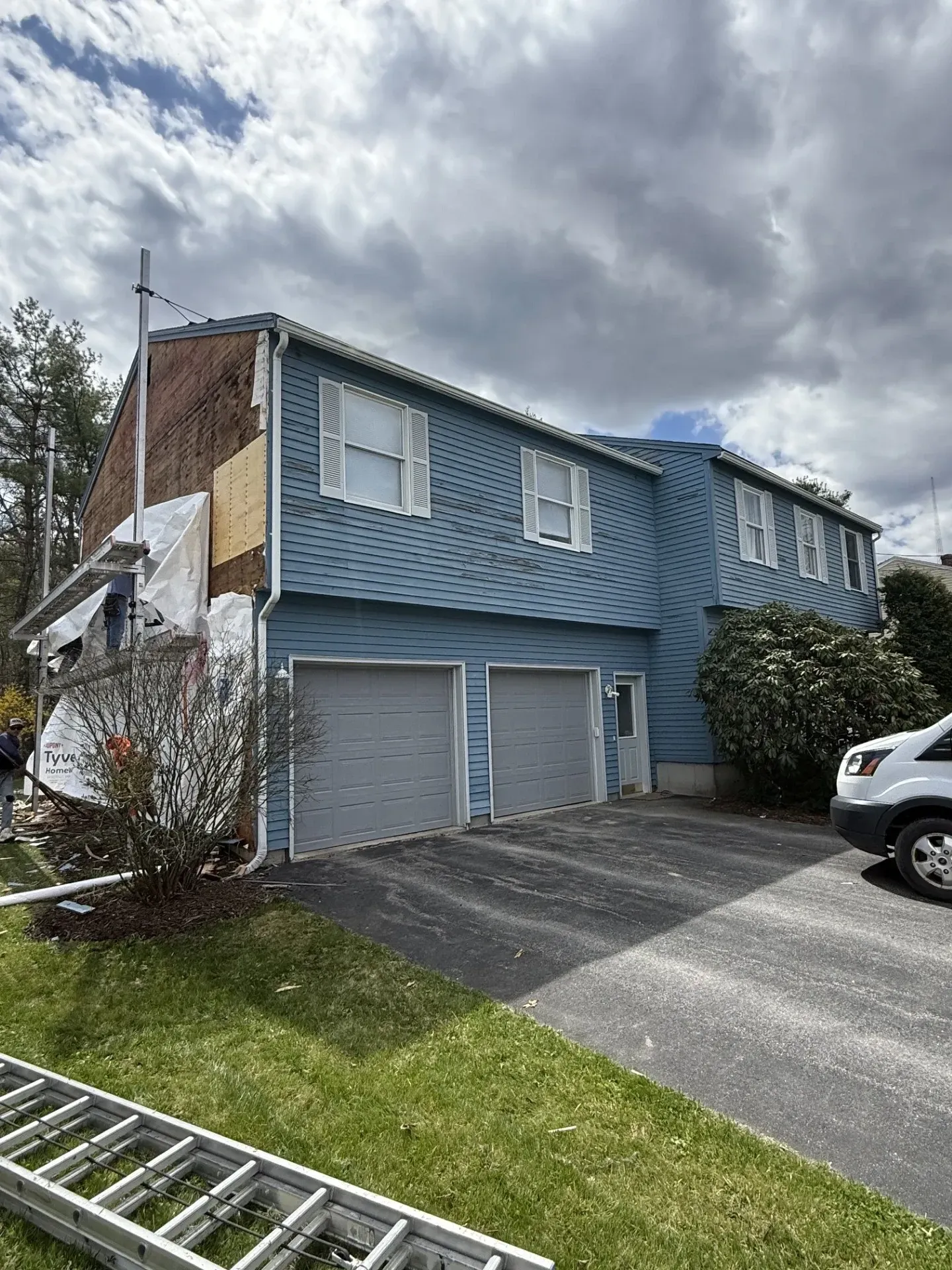 Blue two-story townhouse with garage doors, driveway, and cloudy sky