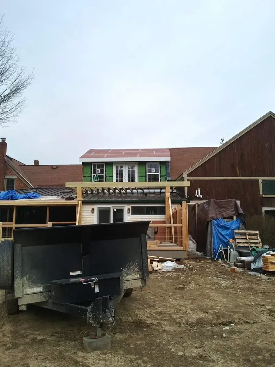 Backyard construction site with dumpster, lumber, tarp-covered materials, and a house under renovation