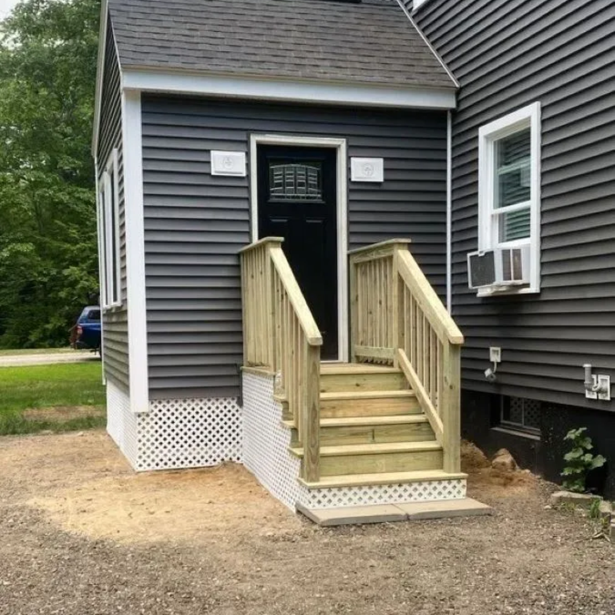 Front entrance with short wooden stairs and railings leading to a black door on a gray house