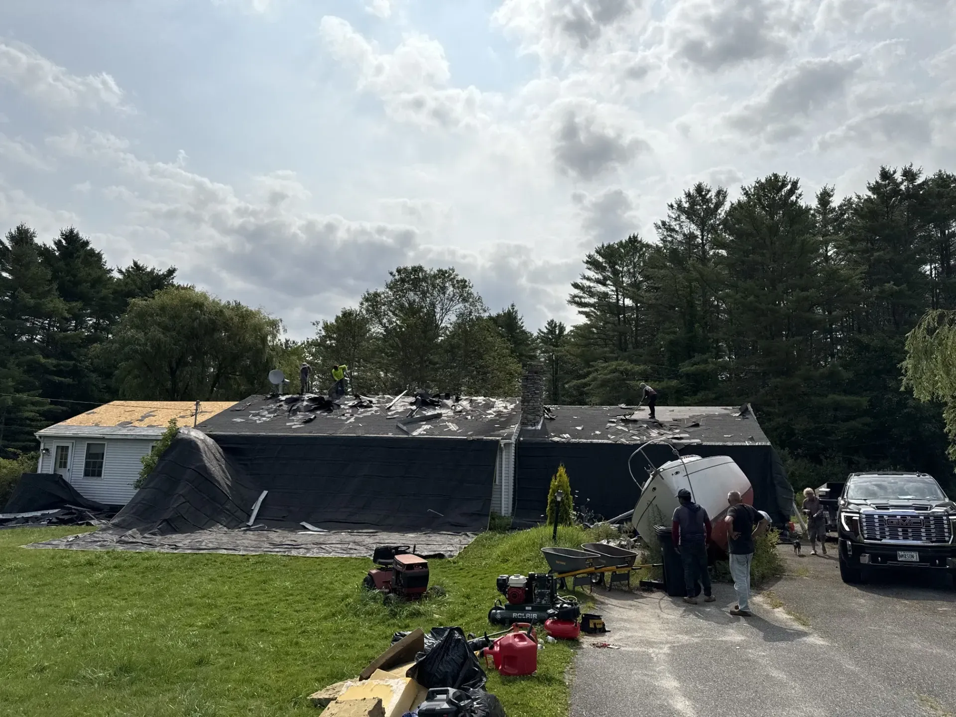 Fire-damaged house with smoke, firefighters, and equipment on a grassy lawn under a cloudy sky