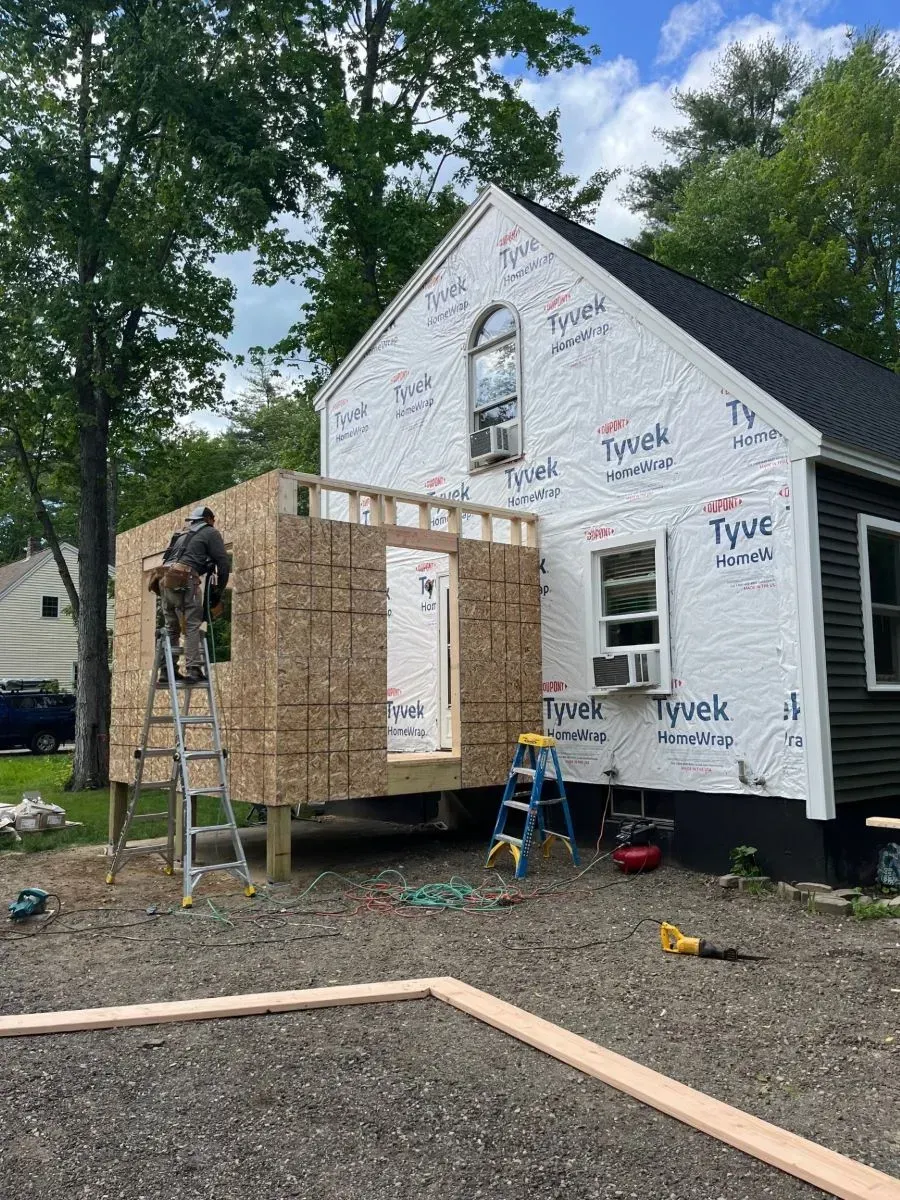 A man is standing on a ladder in front of a house under construction.