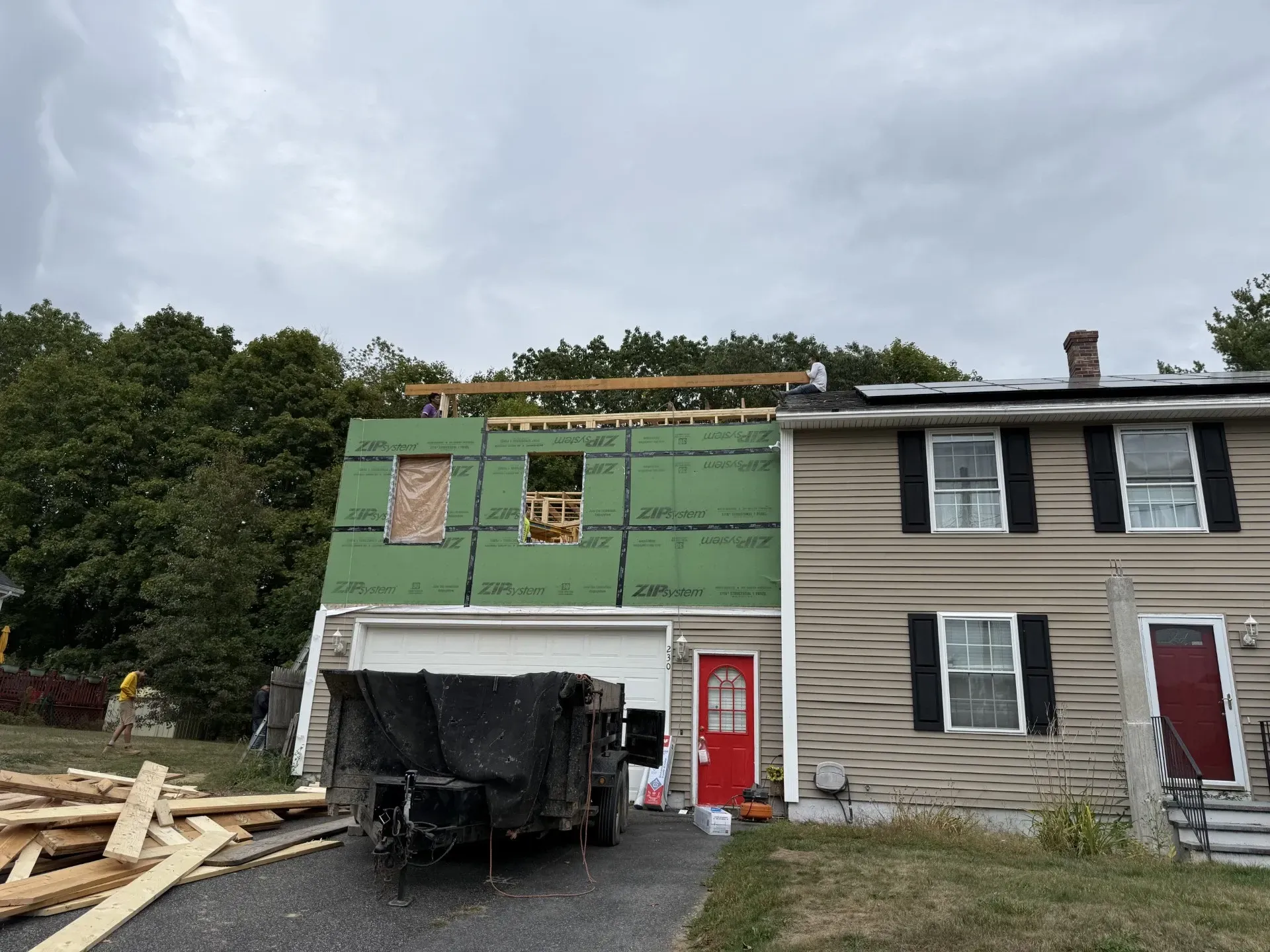 Backyard construction site with dumpster, lumber, tarp-covered materials, and a house under renovation