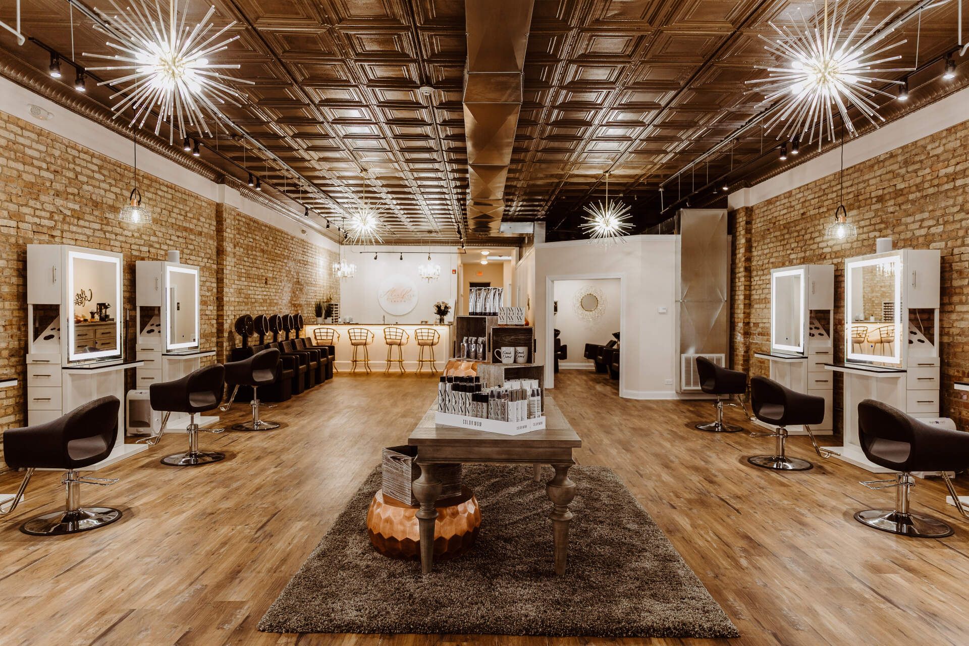 Hair salon interior with styling stations, brick walls, and decorative ceiling lights.