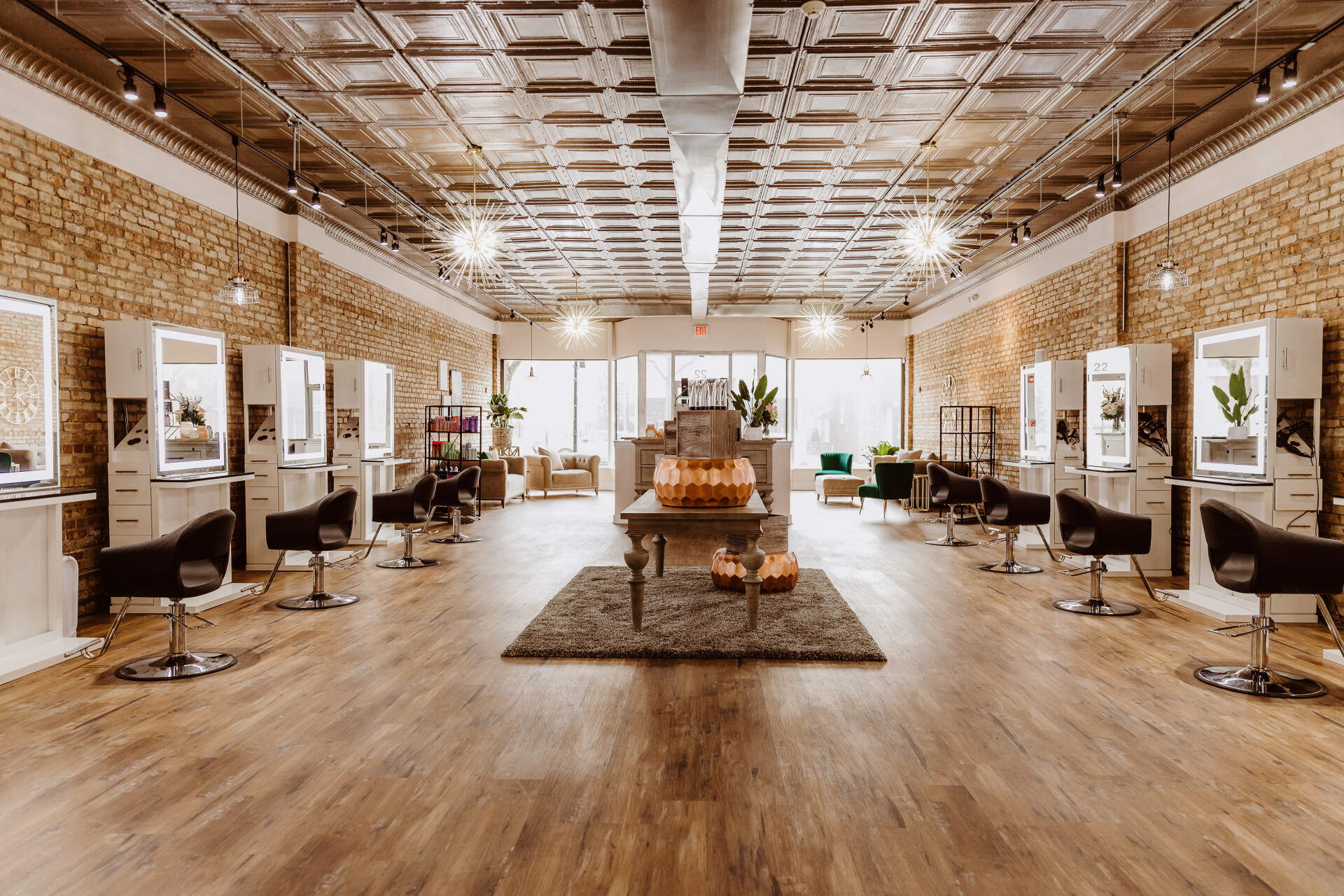 Hair salon interior with brick walls, wood floor, and styling stations with mirrors.