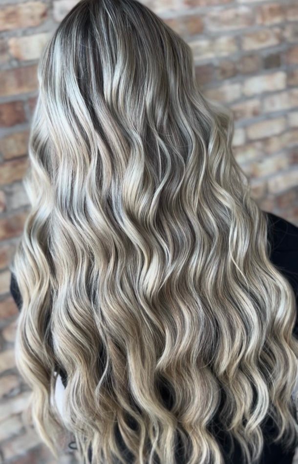 Long, wavy blonde and ash-brown hair with highlights against a brick wall background.