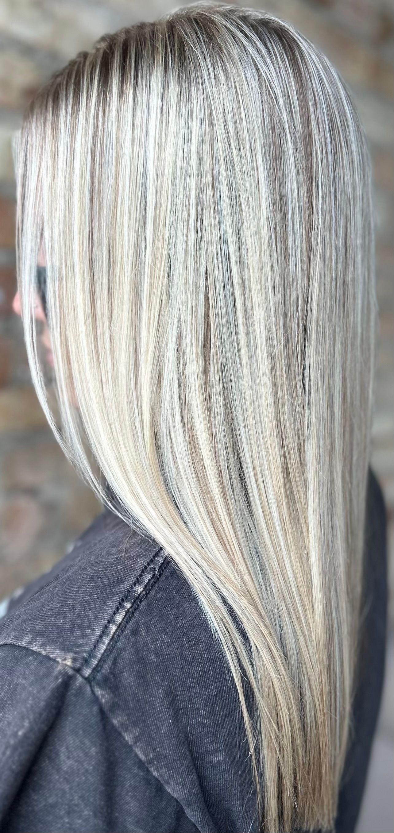 Woman with long, blonde hair that has dark roots. She wears a dark jacket.