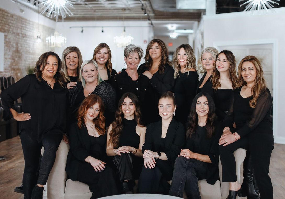 Group of stylists posing together in a modern salon, wearing black outfits.
