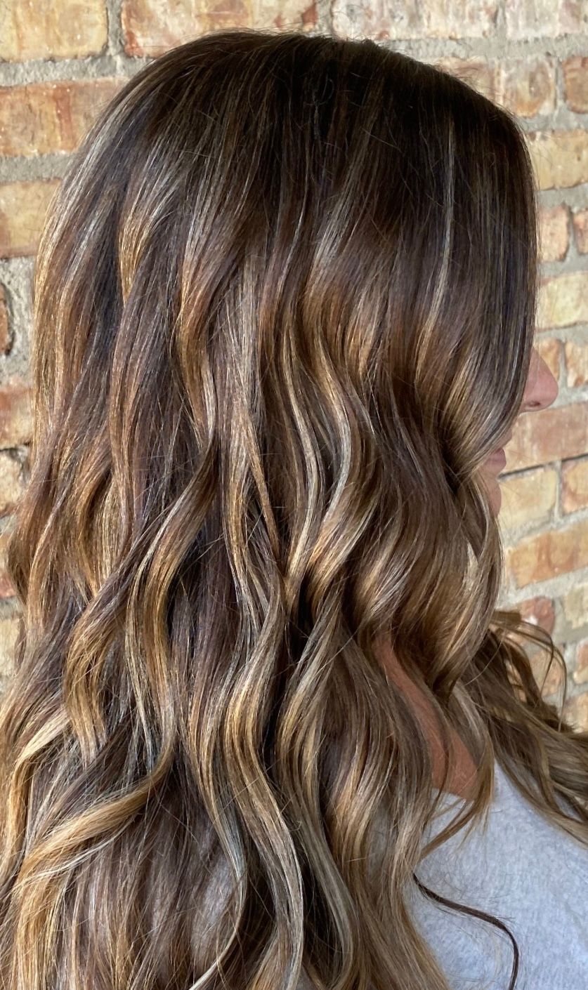 Long, wavy brown hair with blonde highlights against a brick wall.