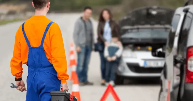 Roadside assistance mobile mechanic carrying a toolbox toward a broken-down car on the highway.