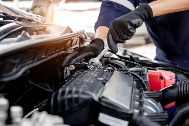 Mechanic wearing protective gloves using a wrench to repair components inside a car engine bay.