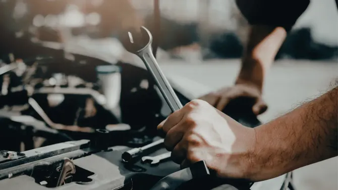 Close-up of a mechanic's hands using a hand spanner wrench to tighten parts on a vehicle engine.