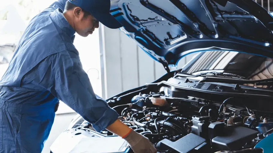 Professional mobile mechanic inspecting a car under the open hood during a routine maintenance service.