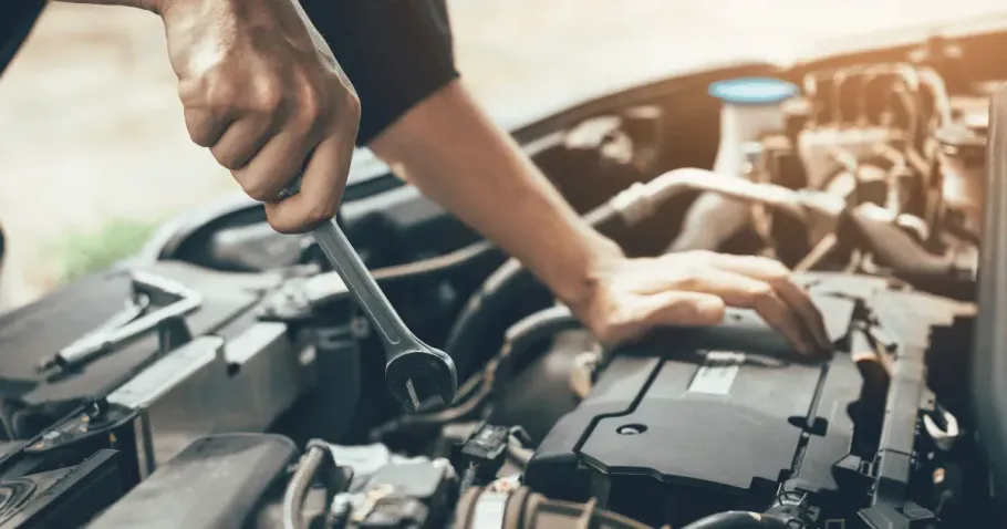 Auto mechanic using a wrench to repair car engine components, ideal for contacting mobile mechanic services.