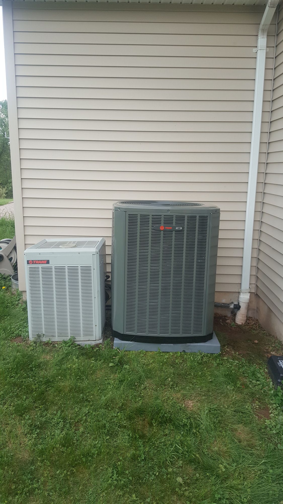 two air conditioners are sitting next to each other on the side of a house .
