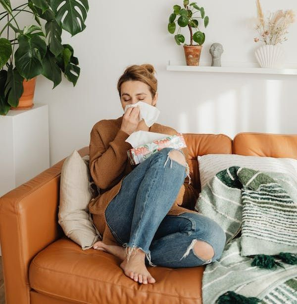 a woman is sitting on a couch blowing her nose with a napkin .