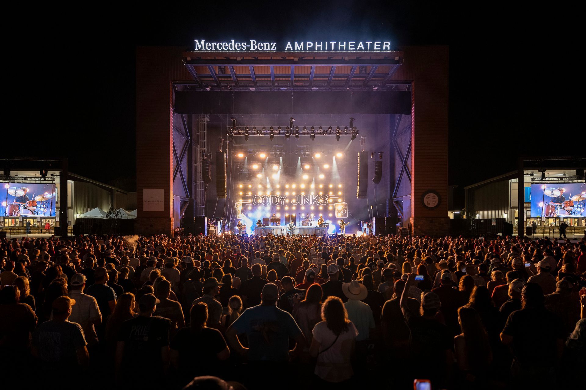 Crowd watching a brightly lit concert stage at an outdoor amphitheater at night