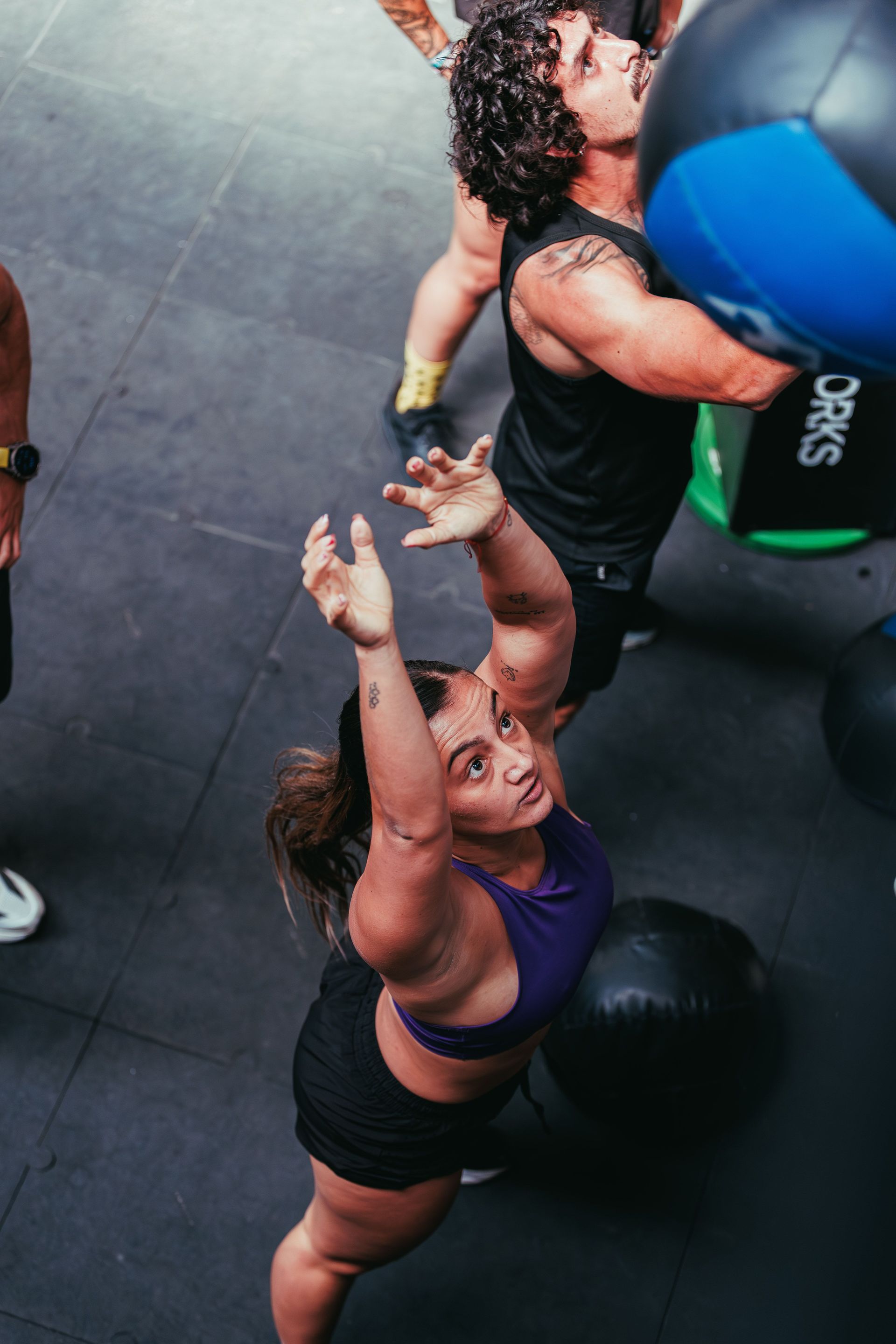 Two people in a gym catch and throw a blue medicine ball during a workout