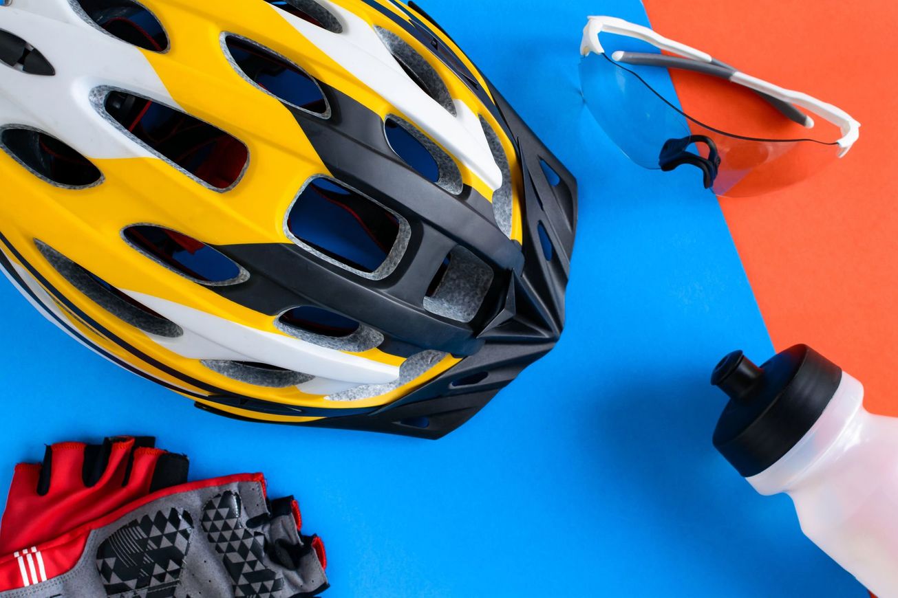 Caschi da bici, guanti, occhiali da sole e borraccia su uno sfondo blu acceso e arancione