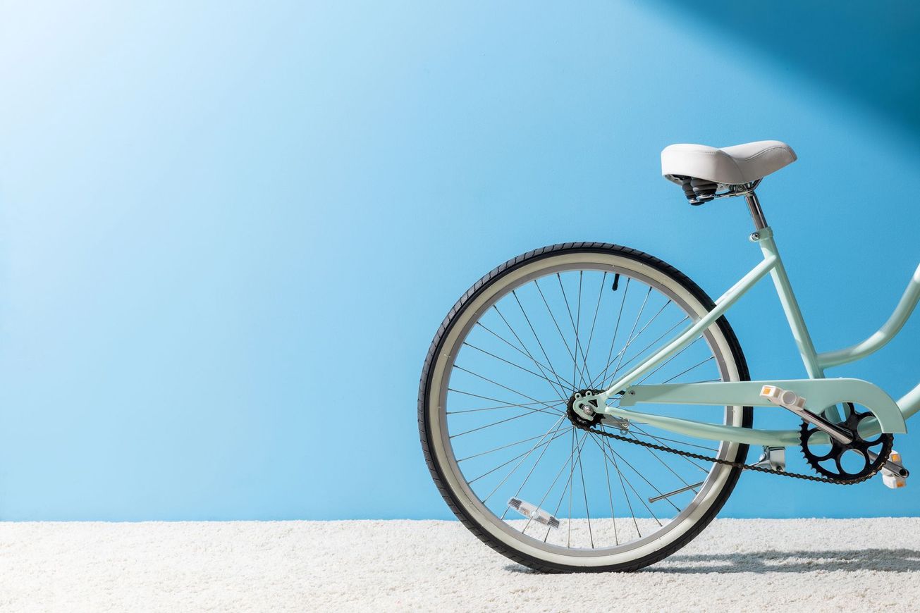 Ruota posteriore di una bicicletta argentata contro una parete azzurra chiara e un pavimento bianco
