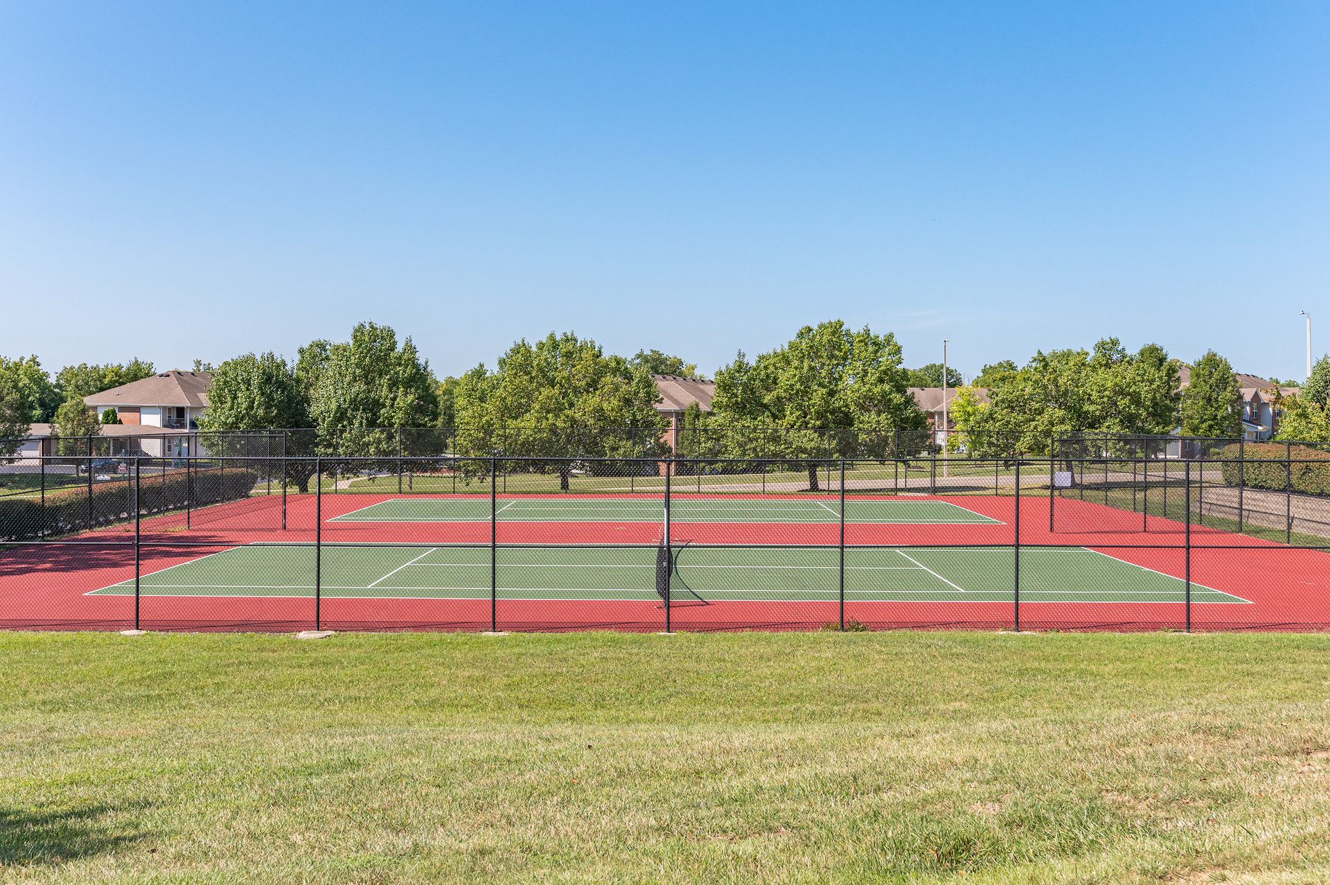 Outdoor tennis court with red surface and fencing at Bridgewater Crossing