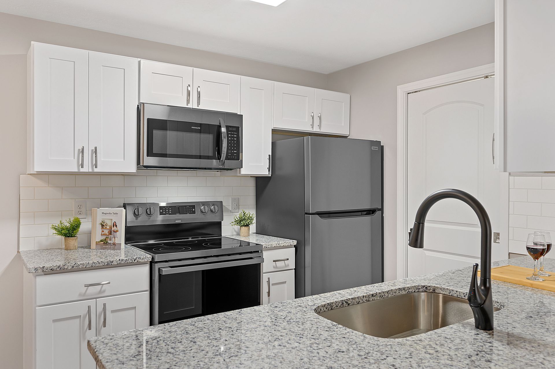 a kitchen with white cabinets , granite counter tops , stainless steel appliances and a black refrigerator .