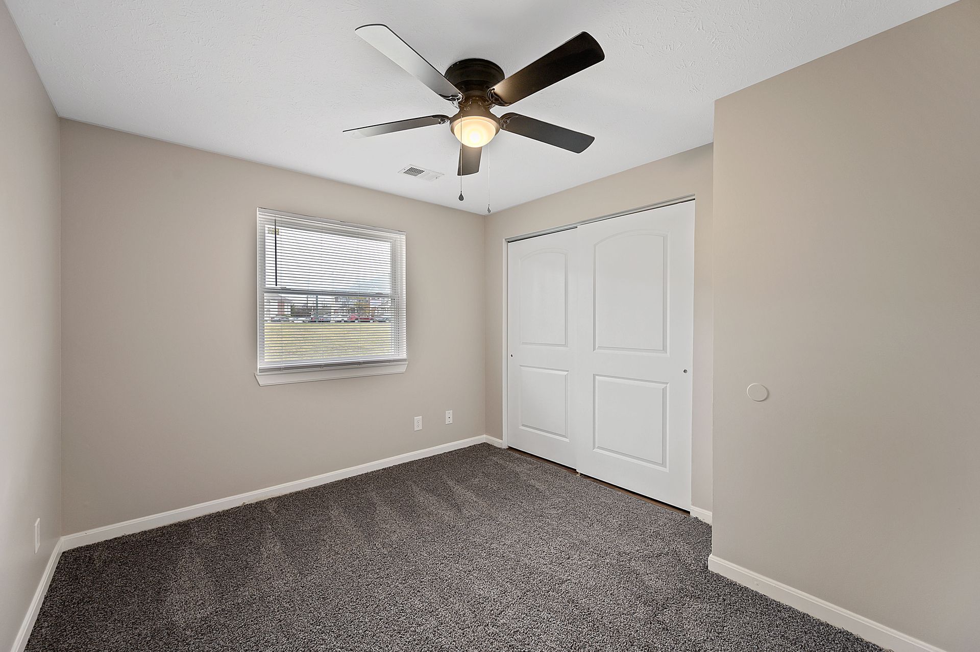 an empty bedroom with a ceiling fan and a window .