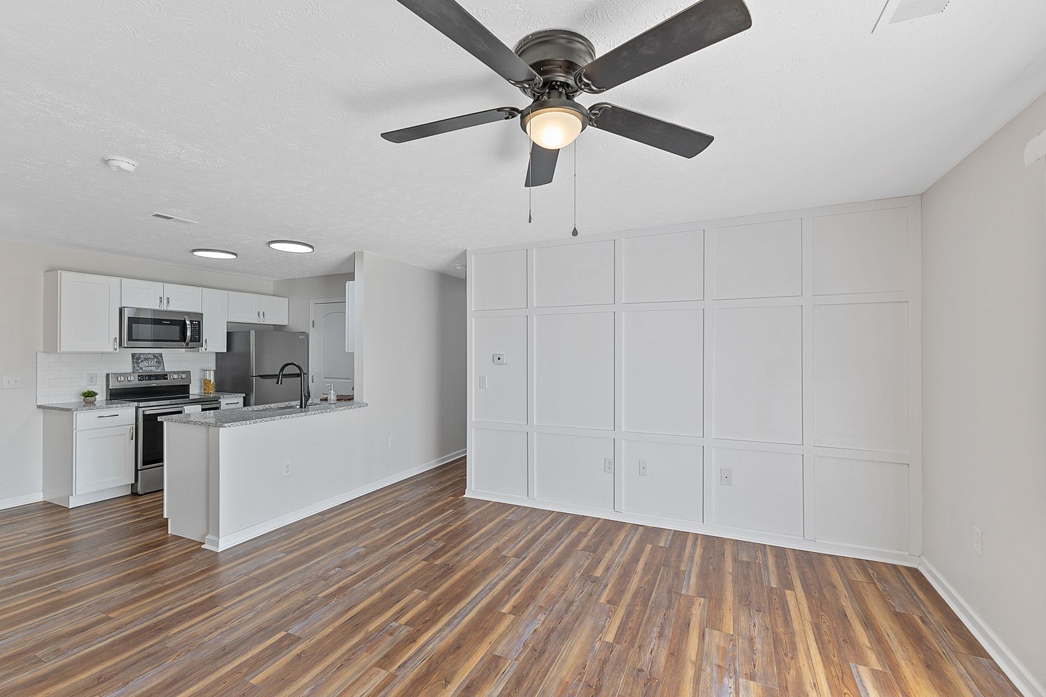 Spacious apartment living area with ceiling fan and hardwood flooring
