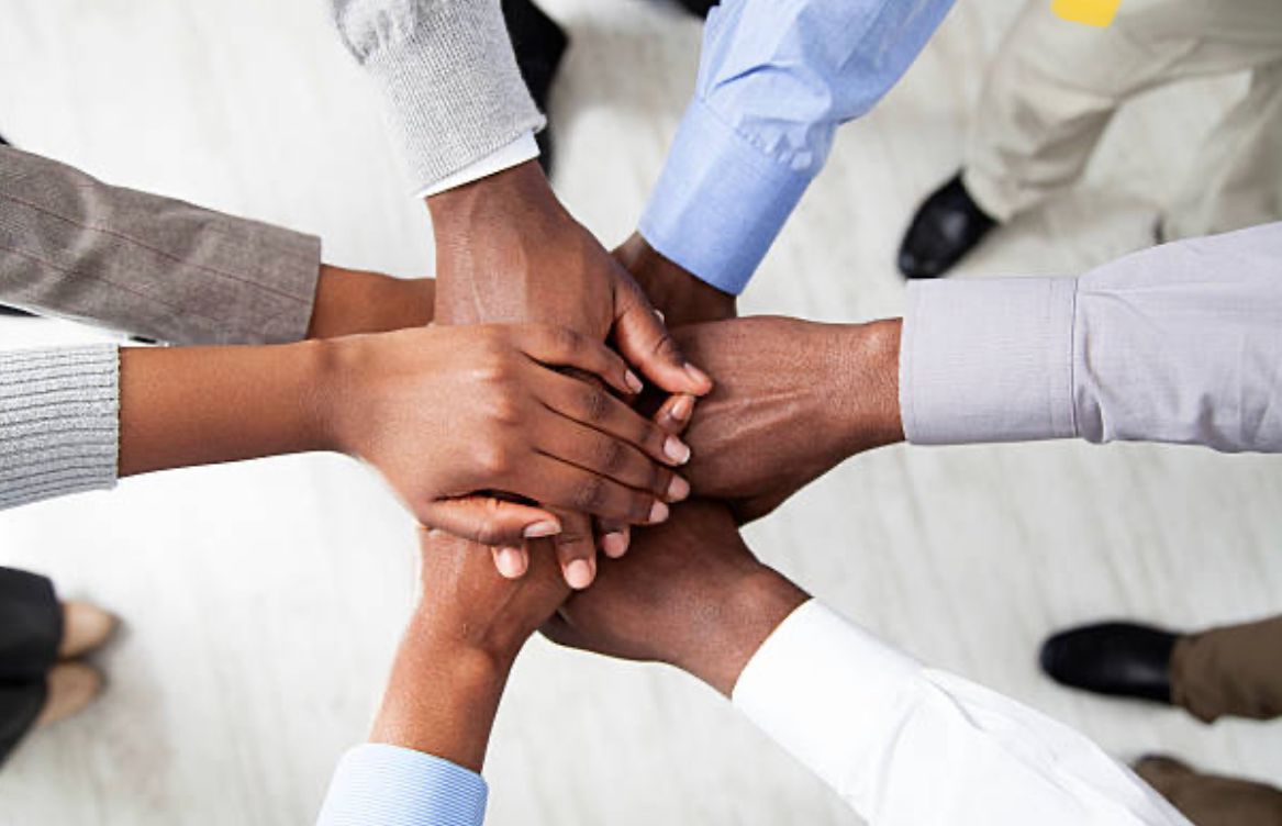 Hands stacked in a team huddle, various skin tones, wearing business attire.