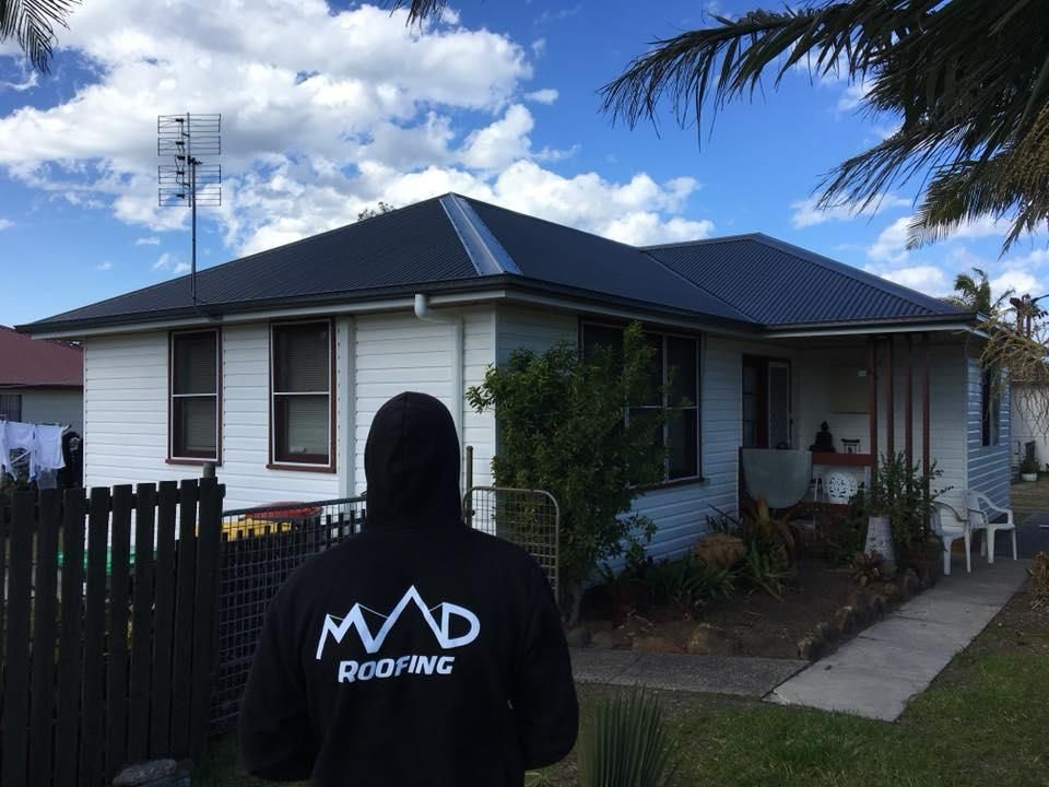 Man On A Hoodie Jacket Looking At The Black Roof — Mad About Metal Roofing & Guttering PTY LTD in Newcastle, NSW