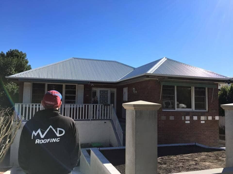A Man Is Standing In Front Of A House With A White Roof — Mad About Metal Roofing & Guttering PTY LTD in Newcastle, NSW