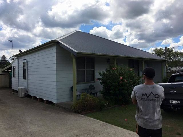A Man Is Standing in Front of A White House — Mad About Metal Roofing & Guttering PTY LTD in Newcastle, NSW
