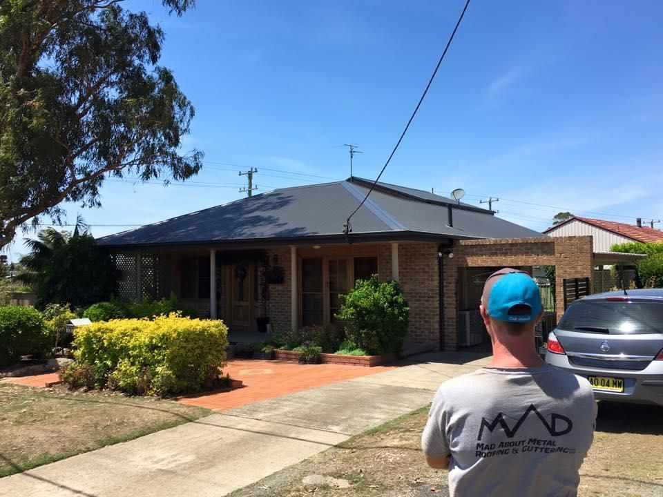 Man Is Looking At The New Black House Roof — Mad About Metal Roofing & Guttering PTY LTD in Newcastle, NSW