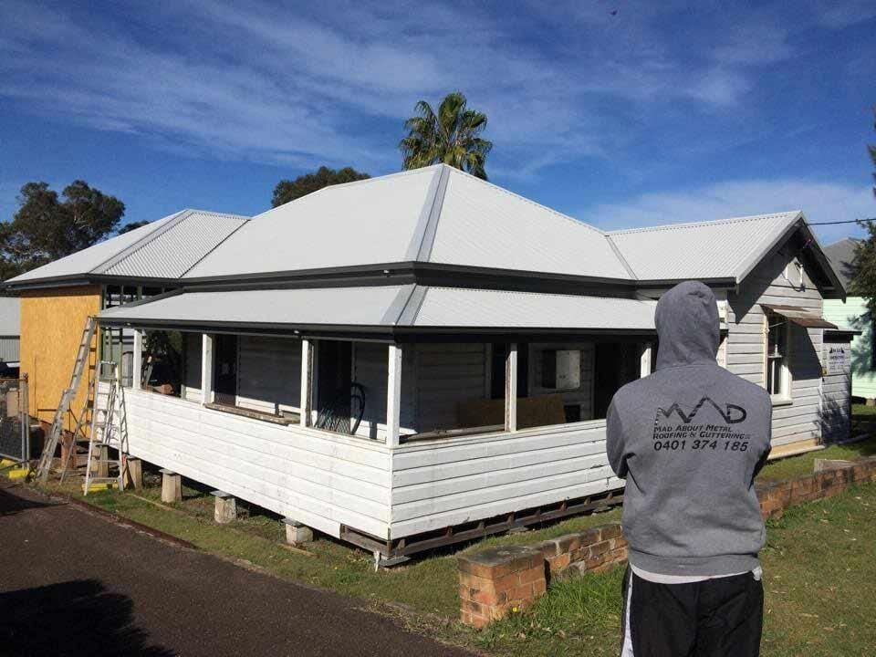 A Man In A Hoodie Is Standing In Front Of A House — Mad About Metal Roofing & Guttering PTY LTD in Newcastle, NSW