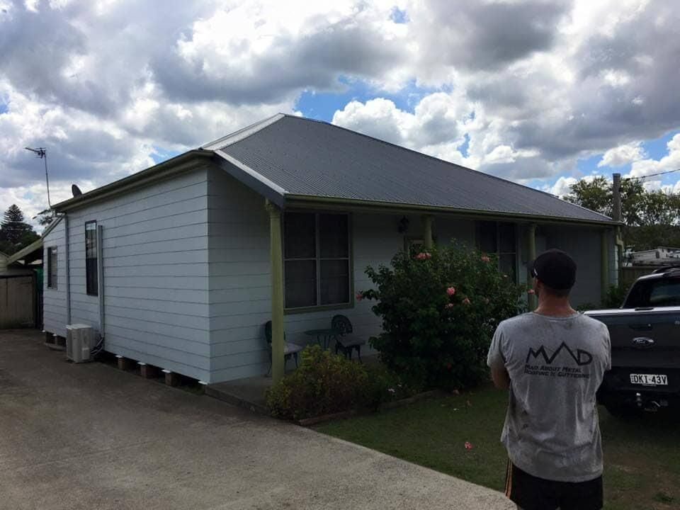 A Man Is Standing In Front Of A White House — Mad About Metal Roofing & Guttering PTY LTD in Newcastle, NSW