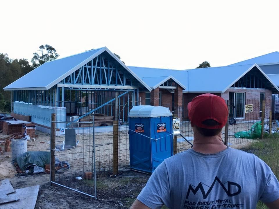 A Man Is Standing In Front Of A House Under Construction — Mad About Metal Roofing & Guttering PTY LTD in Newcastle, NSW