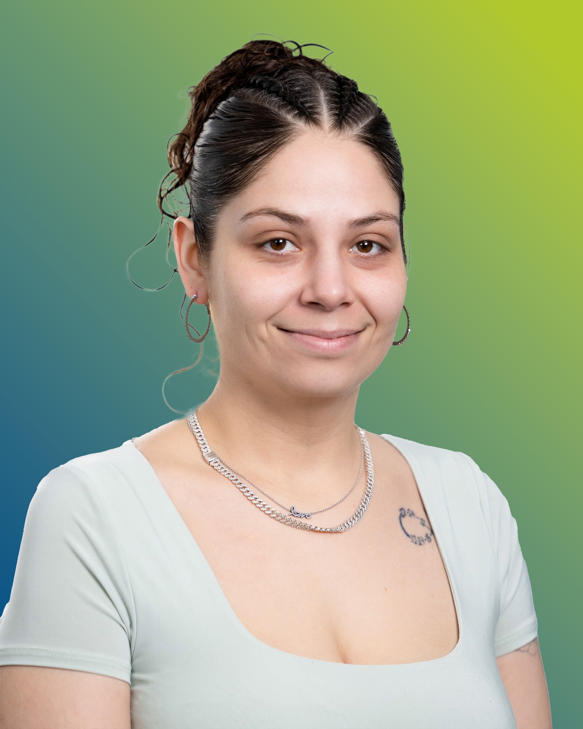 A person with hair pulled back in a high ponytail, wearing a light-colored top, silver chain, and hoop earrings.