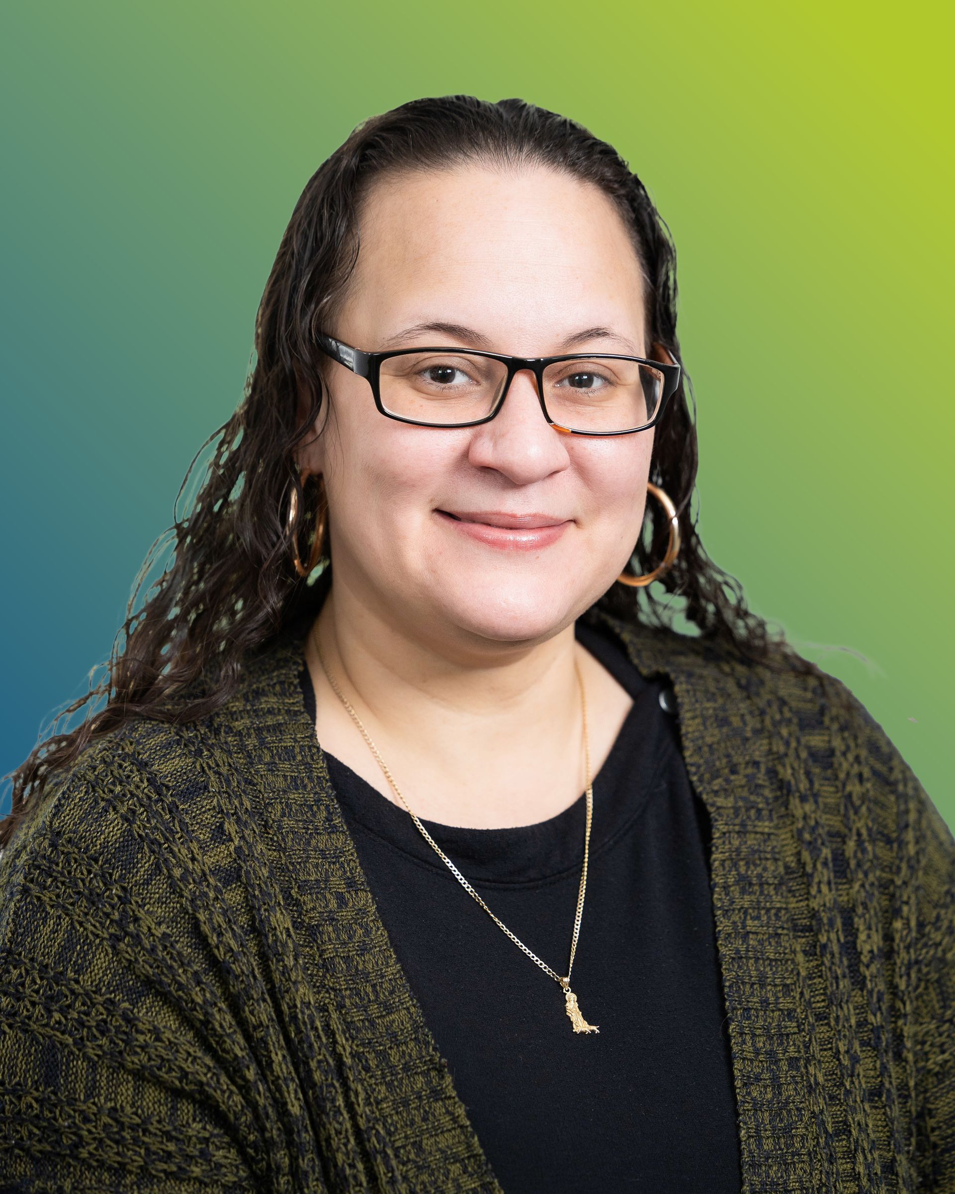 Person with long dark hair and glasses wearing a dark top and olive-green cardigan against a teal to yellow background.