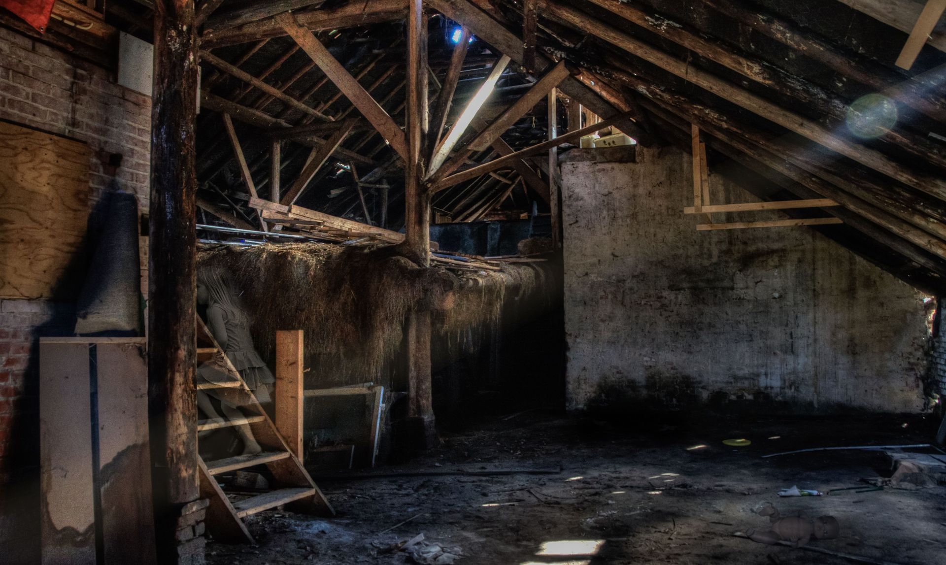 Abandoned barn interior with exposed beams, rough walls, stairs, and sunlight streaming through gaps in the roof