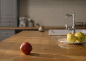 Red apple on a kitchen counter with two yellow apples in the background.
