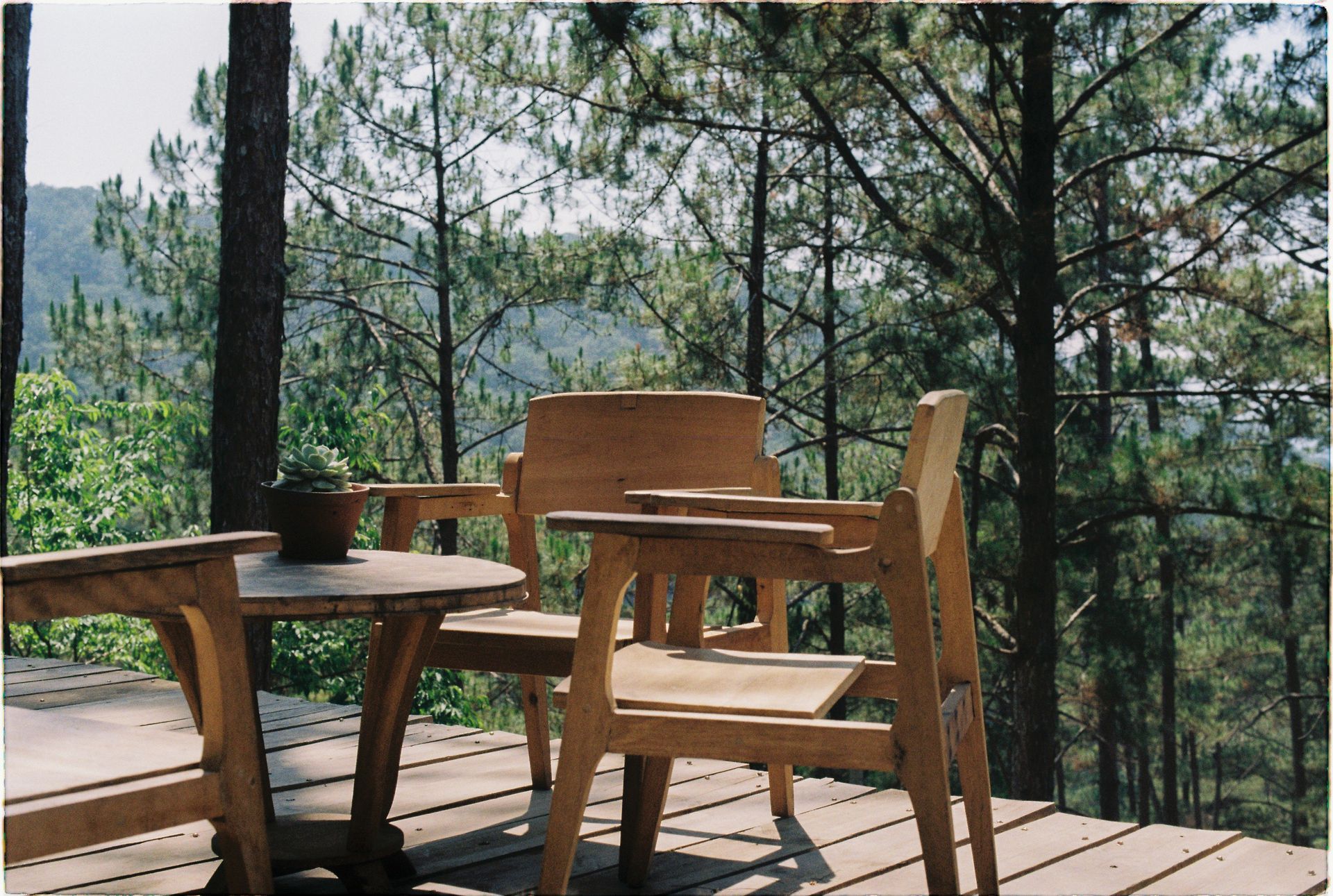 Wooden chairs and a small table on a deck overlooking a wooded mountain view
