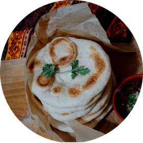 Stack of flatbread in a paper bag, garnished with parsley, next to a small bowl of sauce.