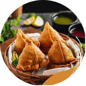 Basket of golden samosas with dipping sauces and lemon slices.