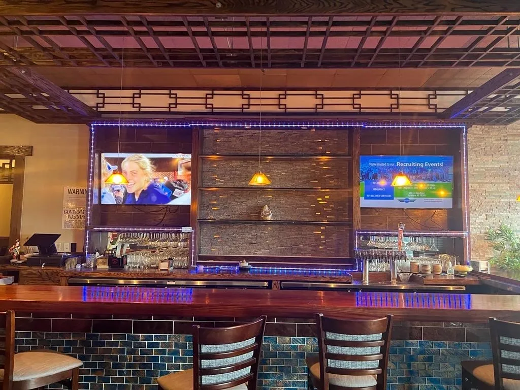 Restaurant bar with TVs and shelving. Brown bar top, blue accents, dark wood trim.