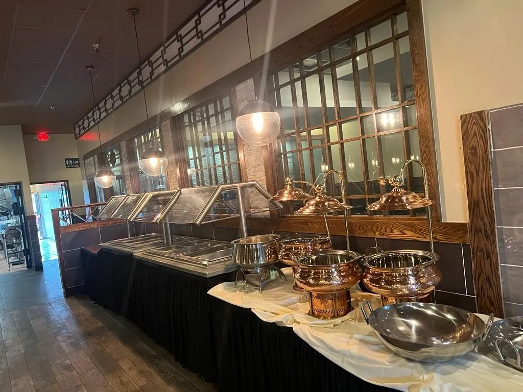 Buffet line with silver and copper serving dishes, under warm lighting, set in a restaurant.