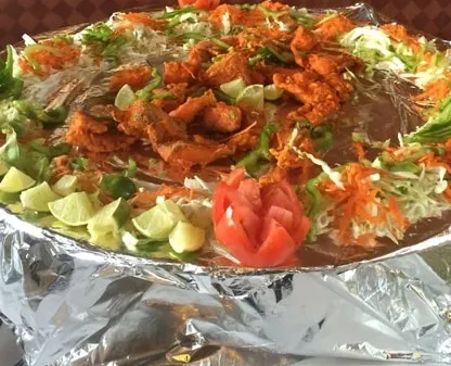 A large platter of fried food, garnished with vegetables and limes, is on a table covered in foil.