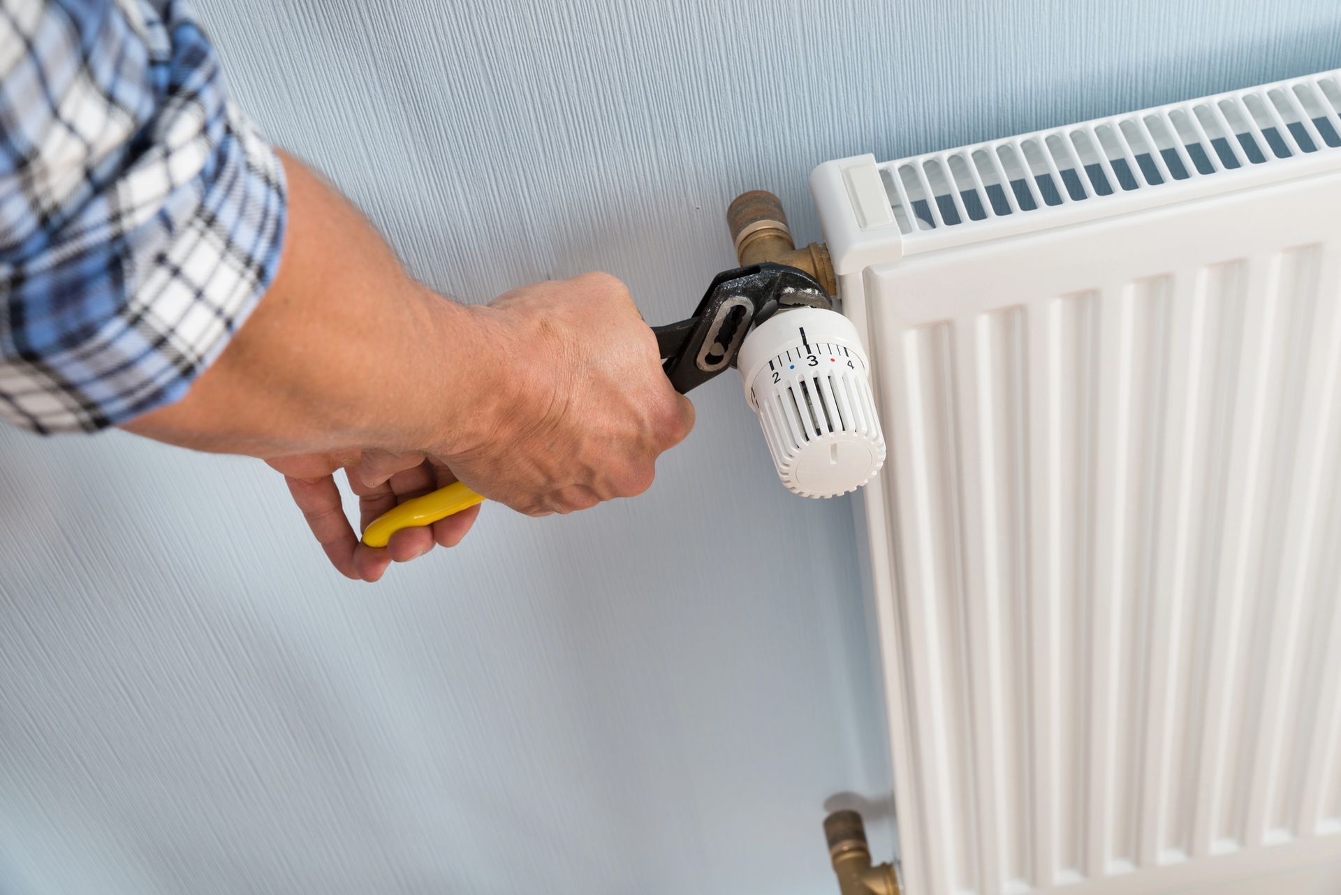 Una persona utiliza una llave inglesa para apretar una válvula en un radiador blanco fijado a una pared azul claro.