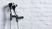 A pair of black forearm crutches leaning against a white brick wall.